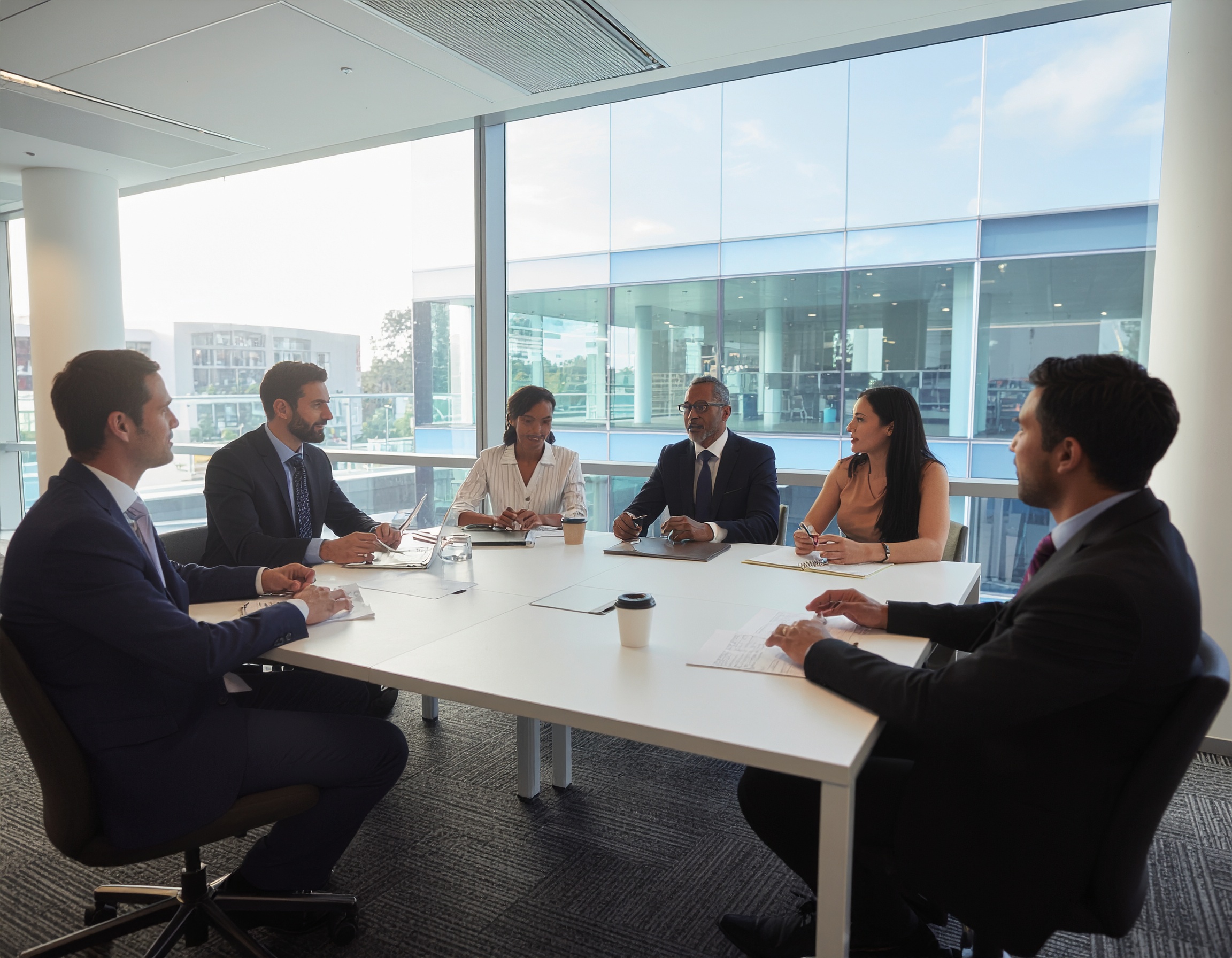 Grupo de profissionais em reunião corporativa em sala de conferências moderna com janelas amplas e luz natural, transmitindo colaboração e foco. Ideal para contextos de negócios e networking.